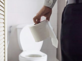 Man holding tissue paper standing next to toilet bowl - health problem concept