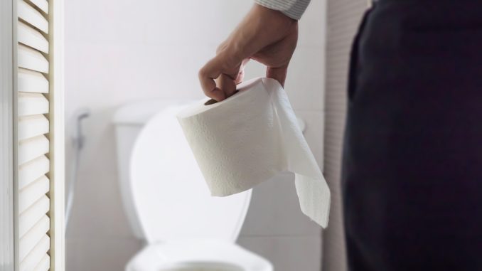 Man holding tissue paper standing next to toilet bowl - health problem concept