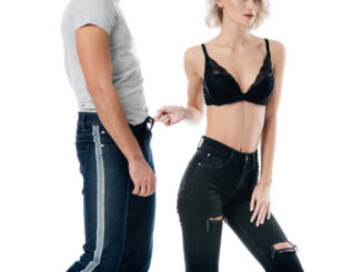 cropped view of woman in bra playfully touching man jeans on white
