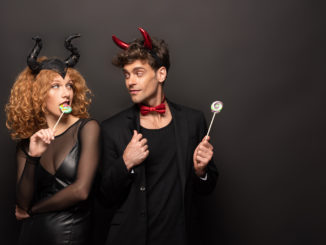 Beautiful couple posing in halloween costumes with sweet lollipops on black