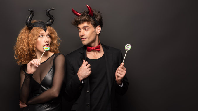 Beautiful couple posing in halloween costumes with sweet lollipops on black