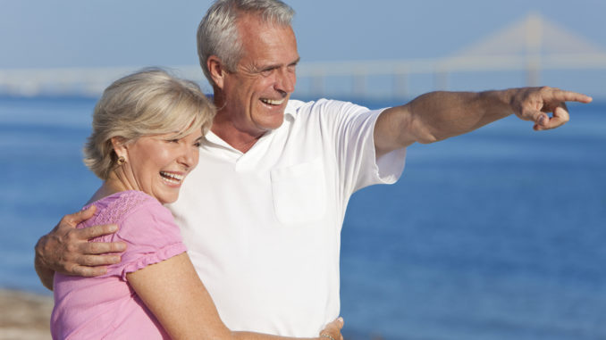 Happy senior men and women couple together walking and pointing on a deserted beach