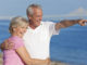 Happy senior men and women couple together walking and pointing on a deserted beach