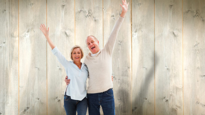 Happy mature couple cheering at camera against pale wooden planks