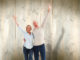 Happy mature couple cheering at camera against pale wooden planks