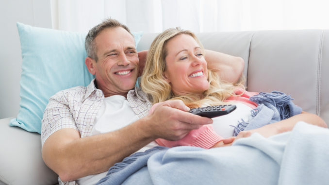 Happy couple cuddling on the couch watching television at home in the living room