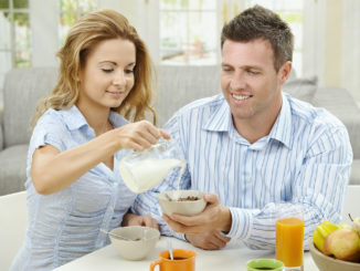 Couple having healty breakfast at home, eating cereals, fruits and drinking orange juice.