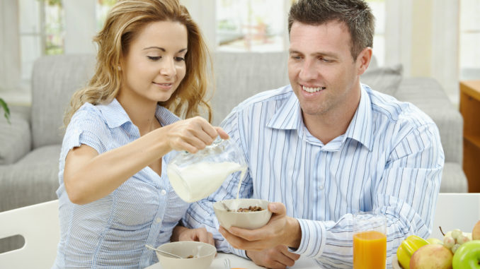 Couple having healty breakfast at home, eating cereals, fruits and drinking orange juice.
