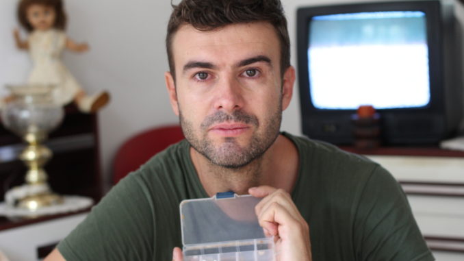 Unhealthy looking man holding pillbox.