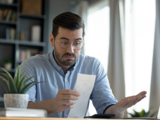 Confused shocked man wearing glasses looking at receipt