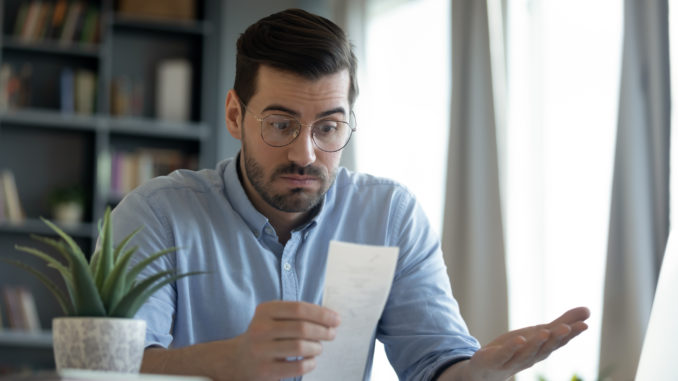 Confused shocked man wearing glasses looking at receipt