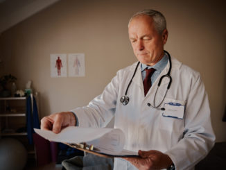 Senior male doctor holding clipboard checking reports in hospital