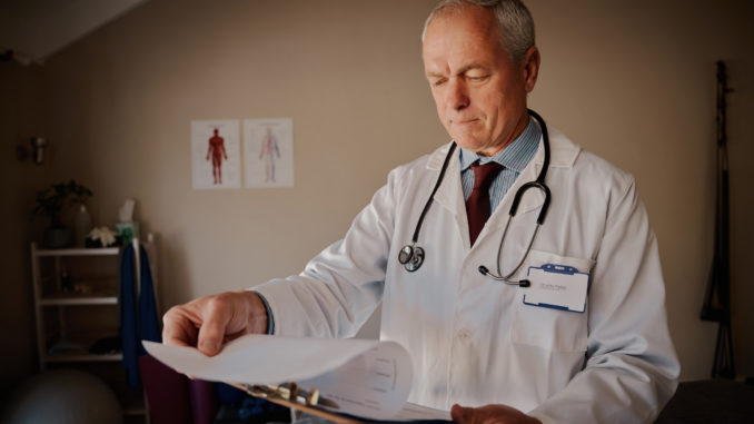 Senior male doctor holding clipboard checking reports in hospital