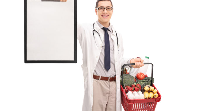 Young doctor holding a shopping basket full of groceries and a clipboard isolated on white background