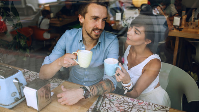 Man talking to women with cup of cappuccino while resting in cafe