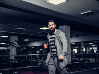 Confident brutal bearded man holding bag and leaving gym after workout looking forward.