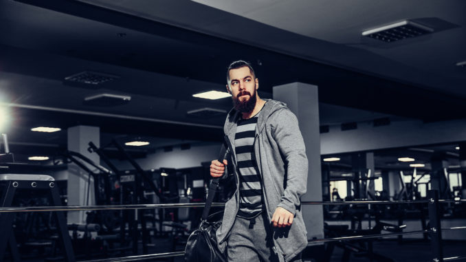 Confident brutal bearded man holding bag and leaving gym after workout looking forward.