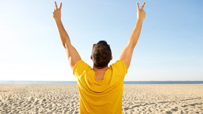 Portrait from back of man cheering with hands raised at the beach