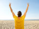 Portrait from back of man cheering with hands raised at the beach