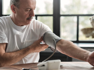 Old hispanic man feeling bad using a home blood pressure machine to check his health in the morning