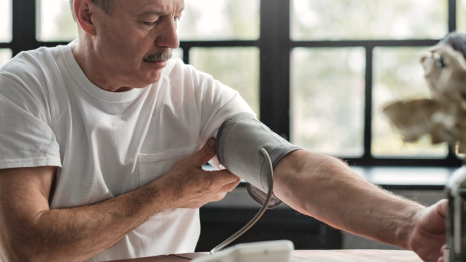 Old hispanic man feeling bad using a home blood pressure machine to check his health in the morning