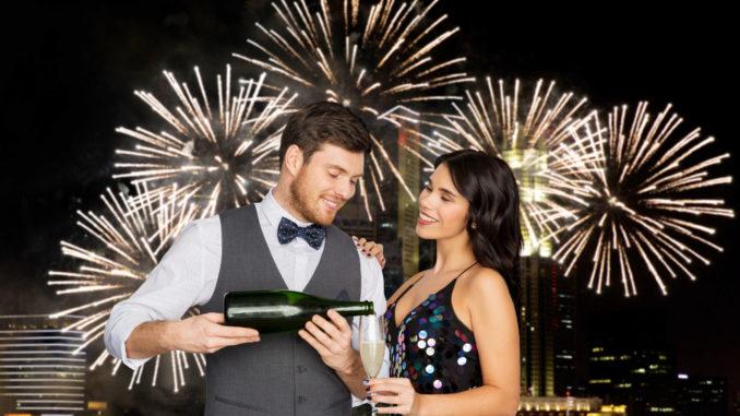 Celebration and holidays concept - happy couple with bottle of non alcoholic champagne and wine glass at party over firework lights at night city background