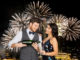 Celebration and holidays concept - happy couple with bottle of non alcoholic champagne and wine glass at party over firework lights at night city background
