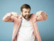 Charming, happy bearded man looks and points his index finger down, smiling broadly and looking at the camera. Isolated on a blue background.