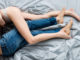Cropped view of men in jeans touching tattooed girlfriend in panties on bed