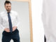 Dissatisfied chubby man in formal wear looking at mirror on white with copy space