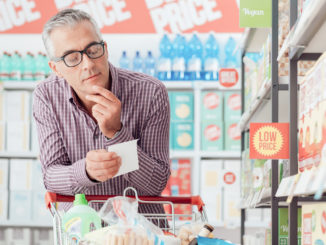 Man doing grocery shopping at the supermarket, he is pushing a cart and checking a list