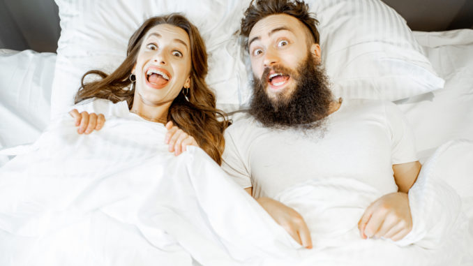 Portrait of a young couple feeling surprised and shocked lying together on the bed under the white sheets