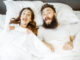 Portrait of a young couple feeling surprised and shocked lying together on the bed under the white sheets