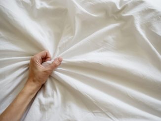 Close up woman hand pulling and squeezing white sheets in ecstasy in bed.