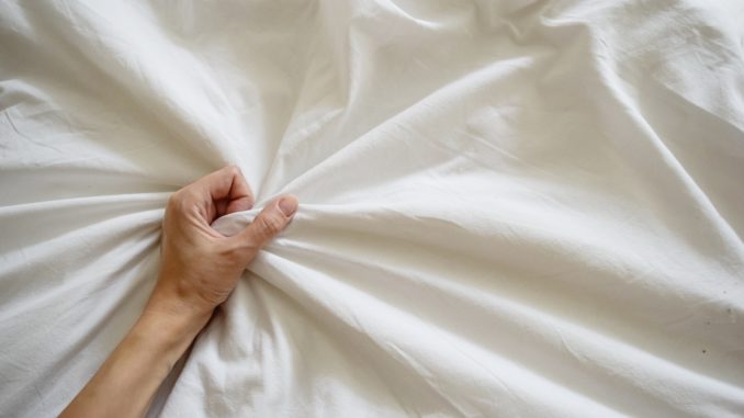 Close up woman hand pulling and squeezing white sheets in ecstasy in bed.