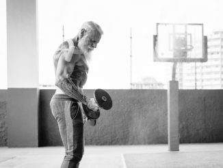 Senior fitness man doing biceps curl exercises inside old gym