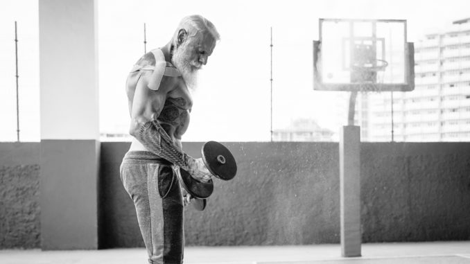 Senior fitness man doing biceps curl exercises inside old gym