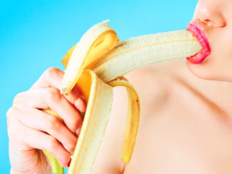 Close-up of woman eating banana isolated on blue.