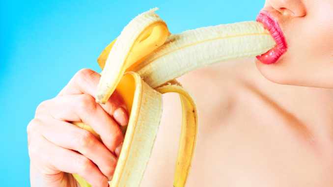 Close-up of woman eating banana isolated on blue.