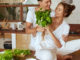 Couple At Kitchen. Romantic Man Giving Bundle Of Herbs