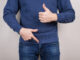 Cropped close-up photo of satisfied confident cool guy demonstrating pointing on his he organ in pants trousers isolated grey background.