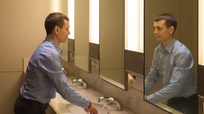 A 35-40 year old man is washing himself in the toilet looking at himself in the mirror