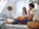 A young couple enjoying eating oranges during a breakfast in the bed at their bedroom.