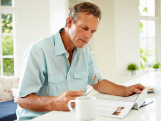 Middle Aged Man Reading Magazine Over Breakfast At Home Concentrating