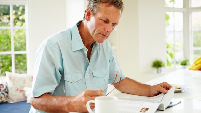 Middle Aged Man Reading Magazine Over Breakfast At Home Concentrating