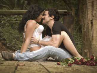 Young attractive couple flirting on wooden deck in forest with red roses