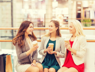 Sale, consumerism and people concept - happy young women with shopping bags and coffee paper cups in mall