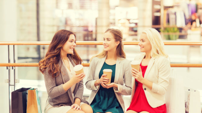 Sale, consumerism and people concept - happy young women with shopping bags and coffee paper cups in mall