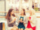 Sale, consumerism and people concept - happy young women with shopping bags and coffee paper cups in mall