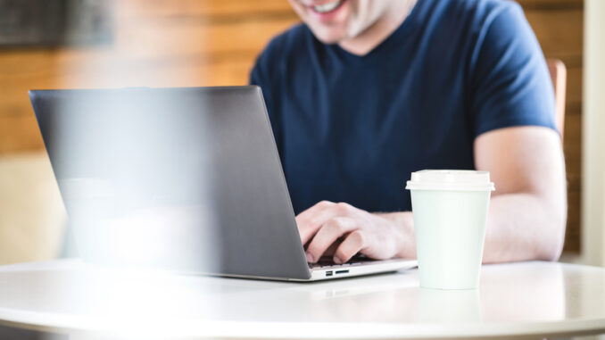 Happy man using laptop with take away coffee cup on table.